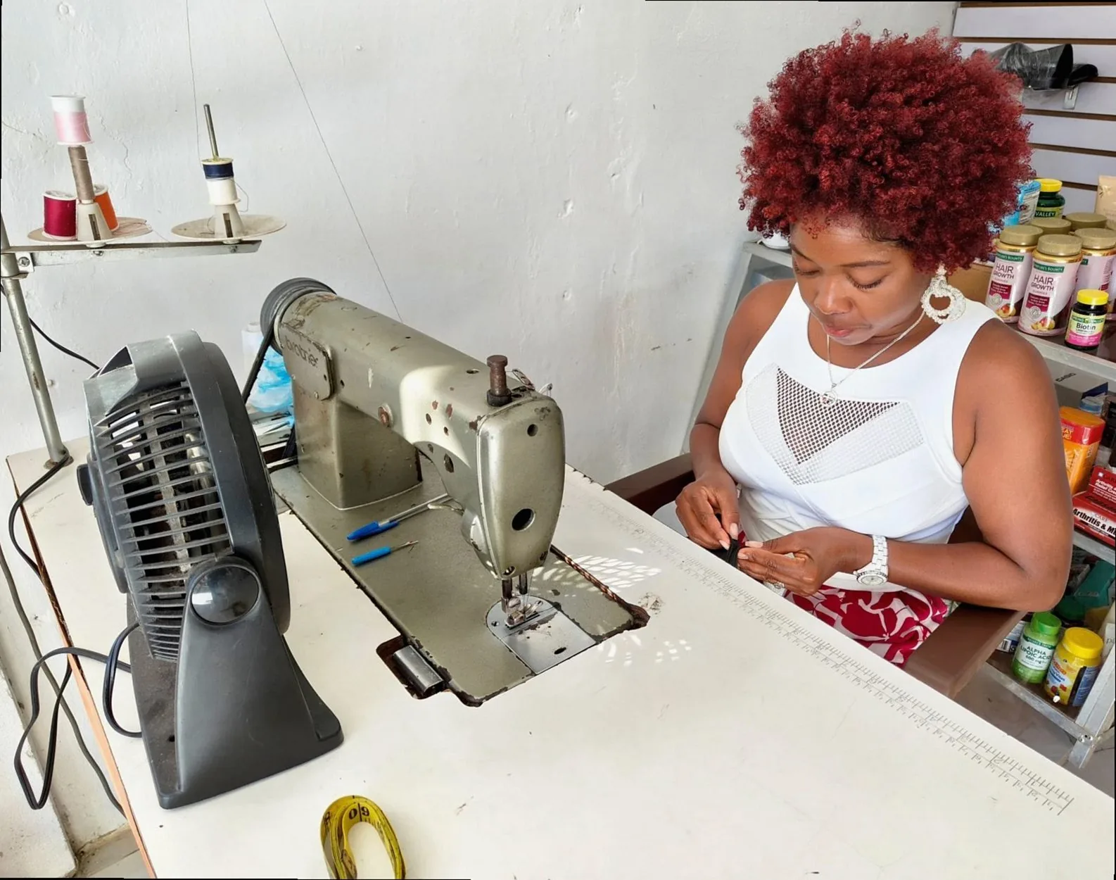 A woman tailor focuses on sewing fabric in a well-equipped sewing shop.