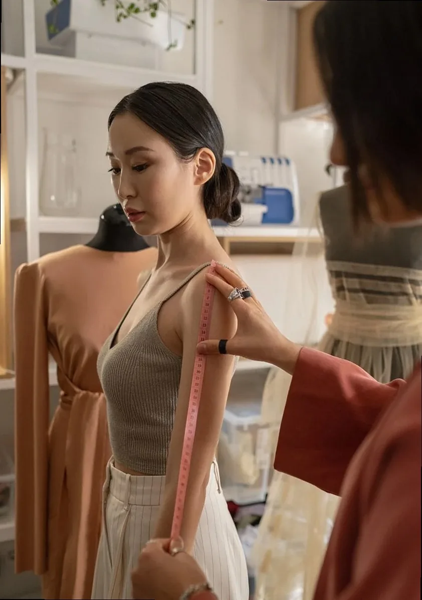 A fashion designer measures a model in a studio for a dress fitting session.